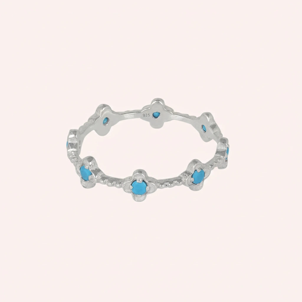 Delicate sterling silver turquoise flower ring with intricate design details on a minimalist light pink background angled view