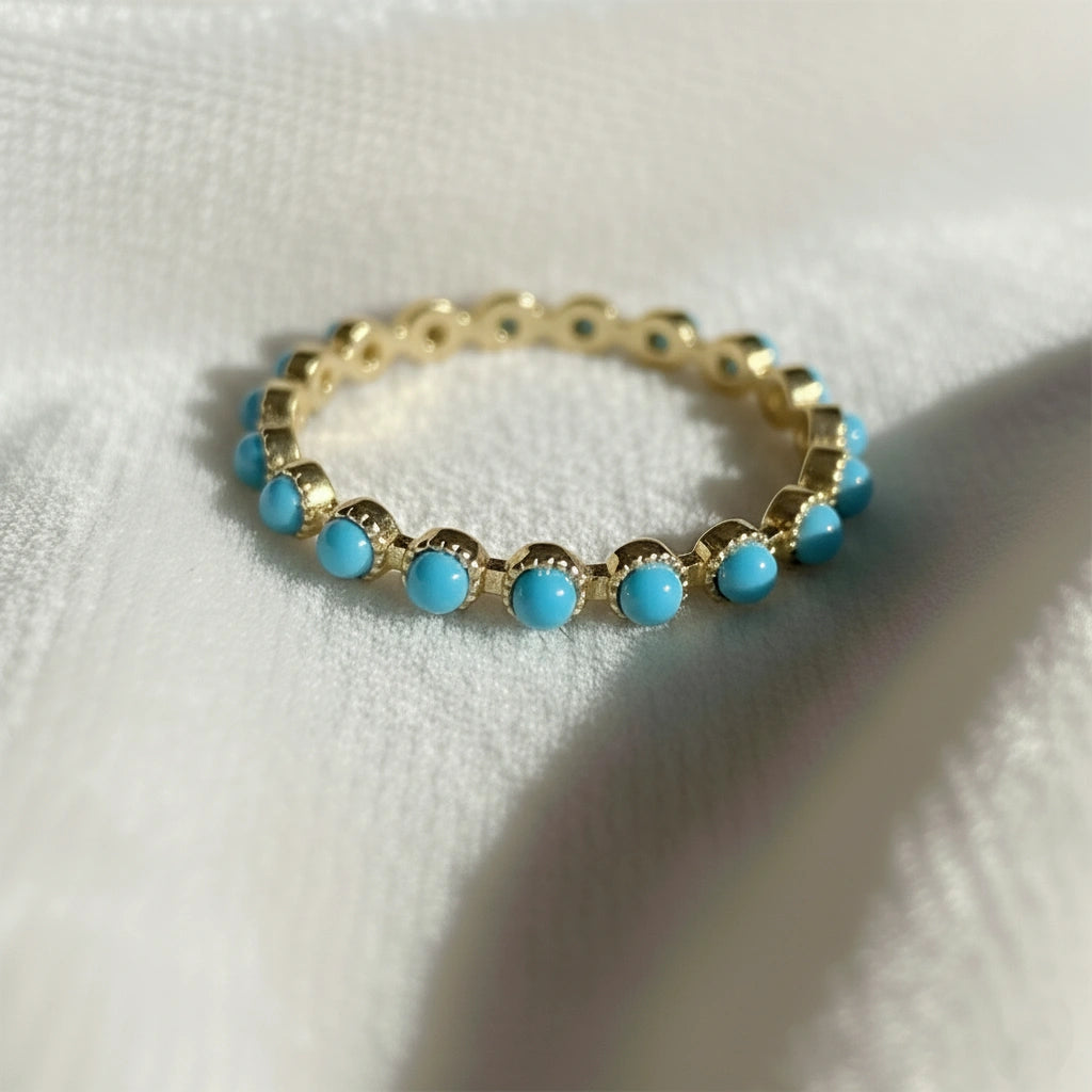 Sterling silver turquoise ring style gold vermeil eternity band with bright blue stones on draped white velvet angled shot.
