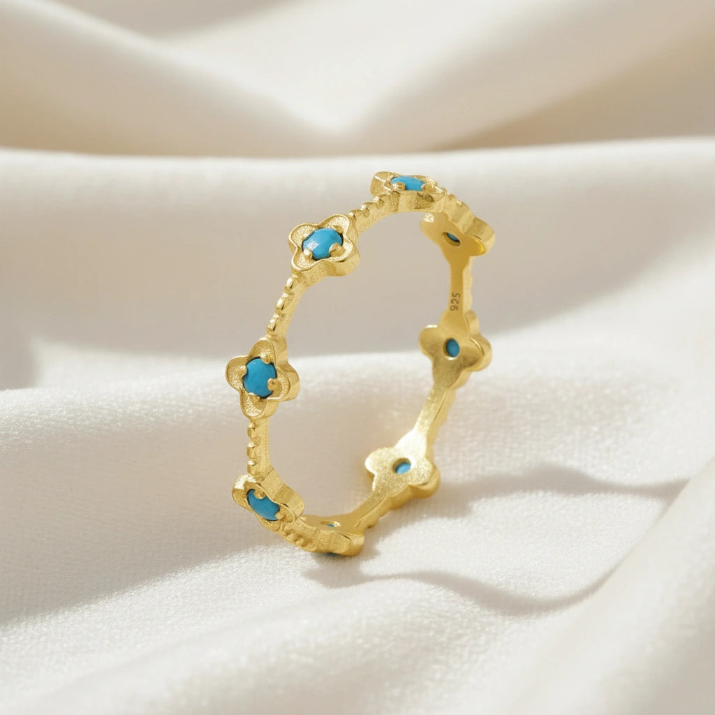 Gold plated flower ring featuring bright turquoise stones on a white velvet cloth soft light angled view highlighting the ring's design.