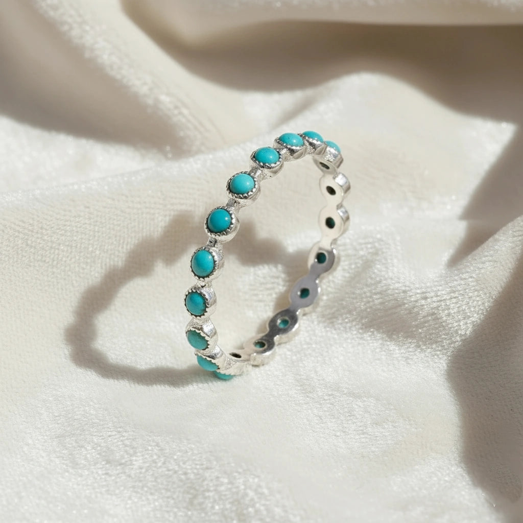 Angled sterling silver turquoise ring a full eternity band featuring round blue turquoise stones on a draped white fabric.