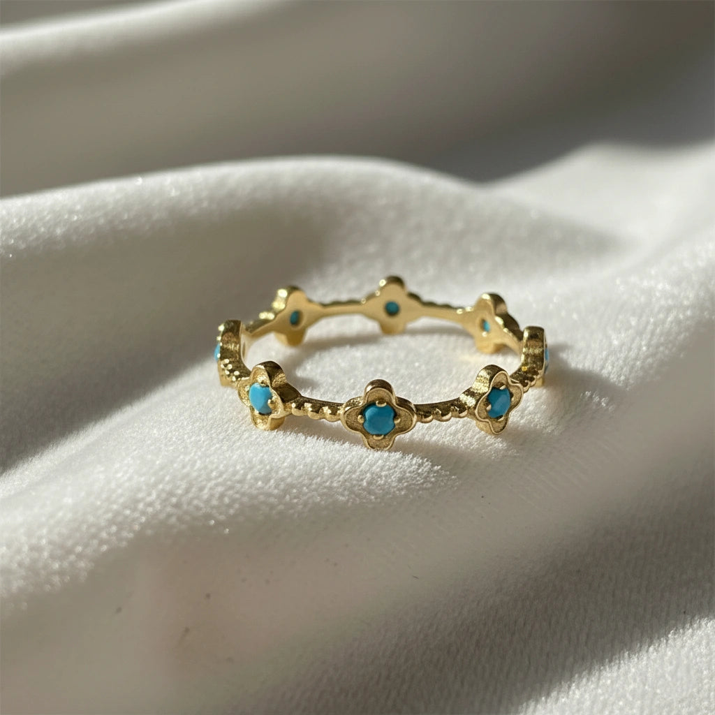 Gold plated flower ring with bright turquoise stones on a white velvet cloth soft light angled view highlighting the ring's design.
