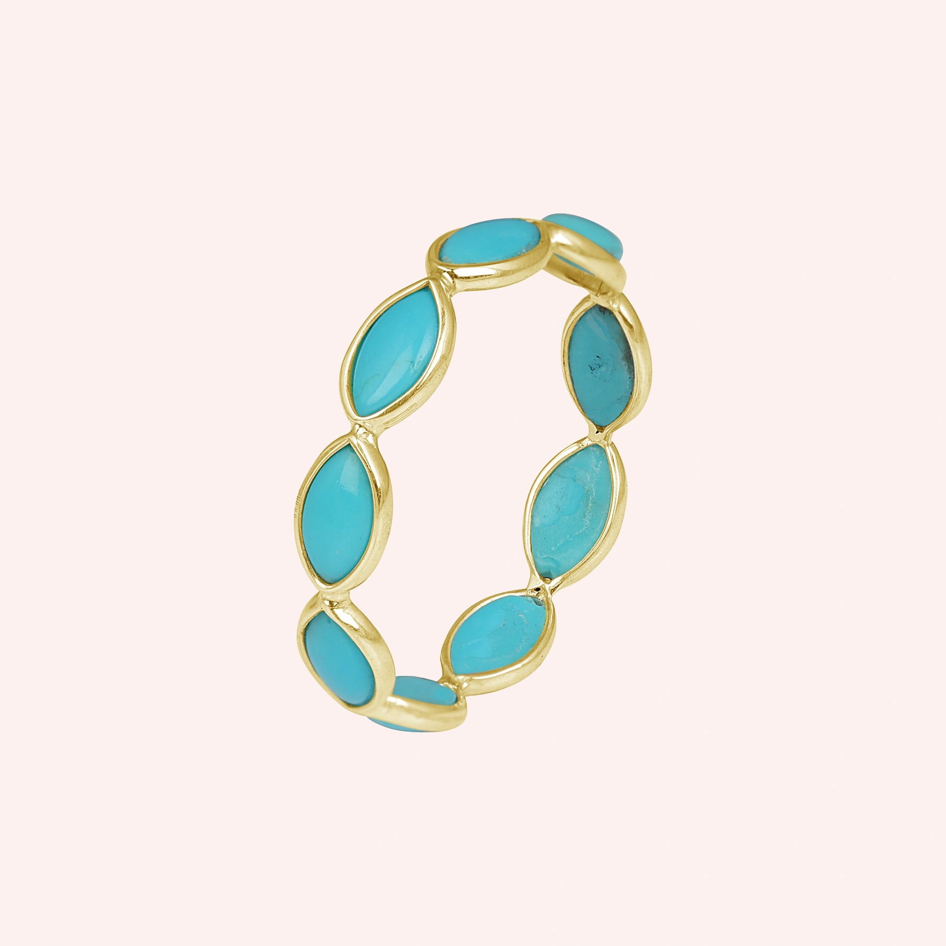 Gold plated silver eternity ring with marquise cut turquoise gemstones set elevated view against light pink background