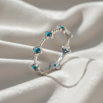 Sterling silver turquoise flower ring with blue turquoise stones on a wrinkled white velvet background viewed at an angle.