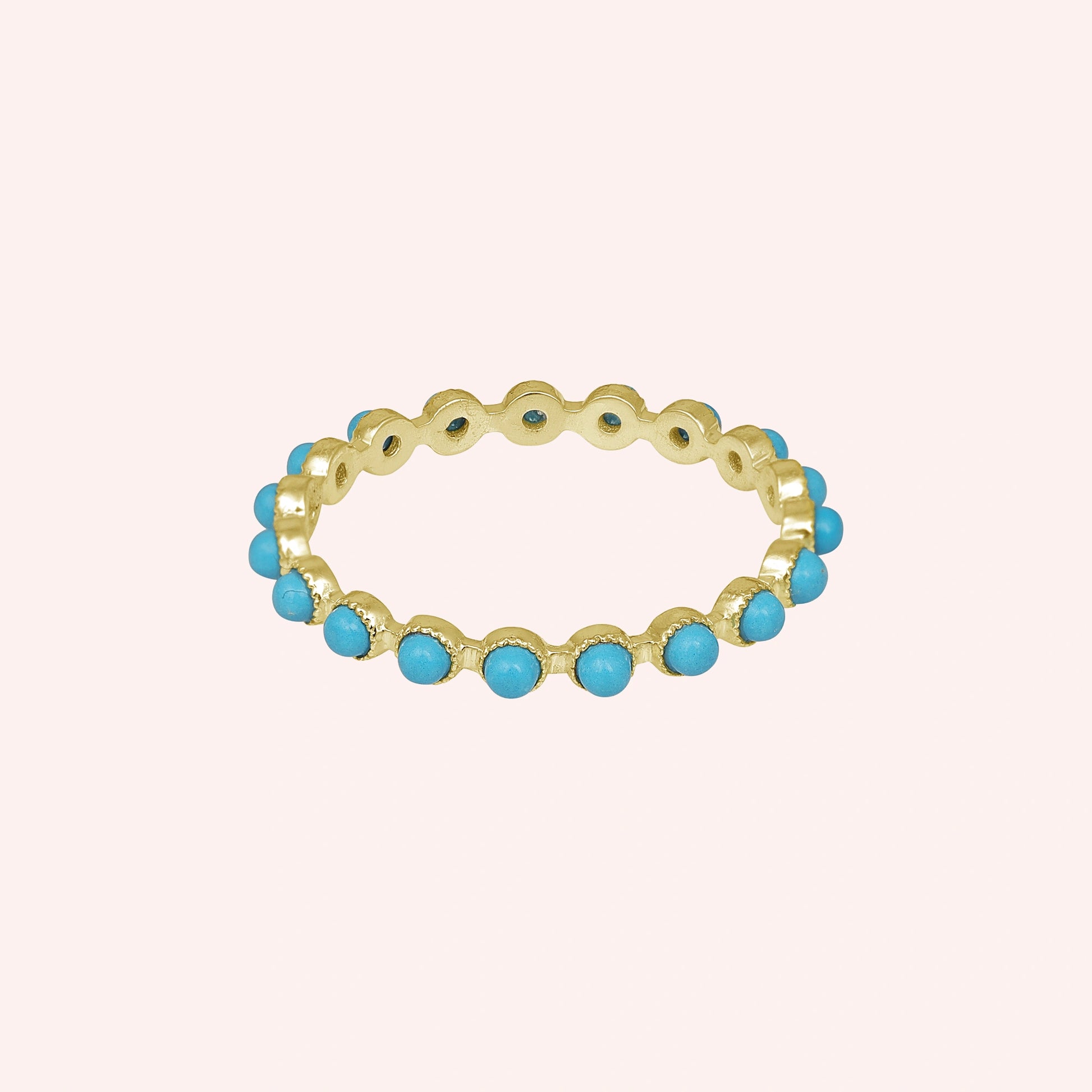 Gold vermeil turquoise ring full eternity band with round blue stones on a light pink background captured in a straight-on view.