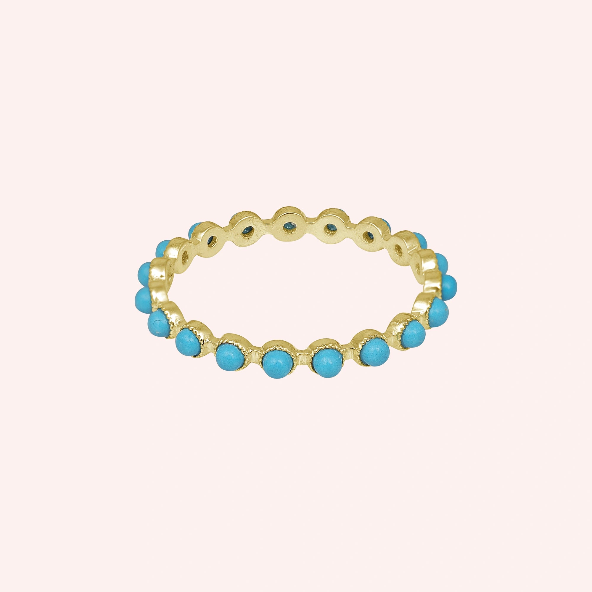 Gold vermeil turquoise ring full eternity band with round blue stones on a light pink background captured in a straight-on view.