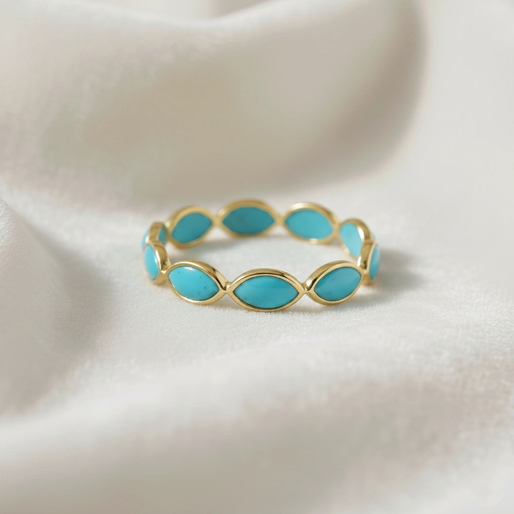 Gold plated silver eternity ring with marquise cut turquoise gemstones elevated view on a white velvet fabric background