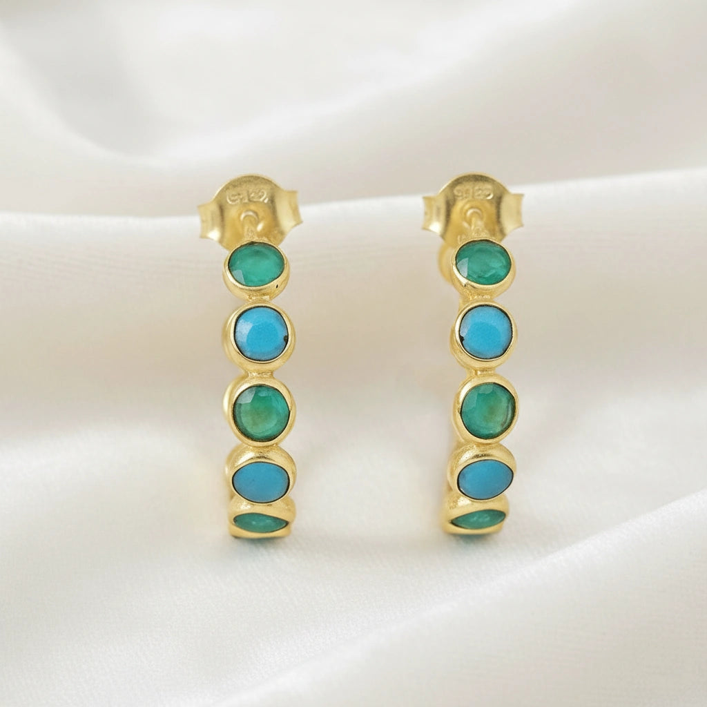 Gold plated sterling silver onyx hoop earrings with bright green stones on a wrinkled cream velvet background angled for detail.