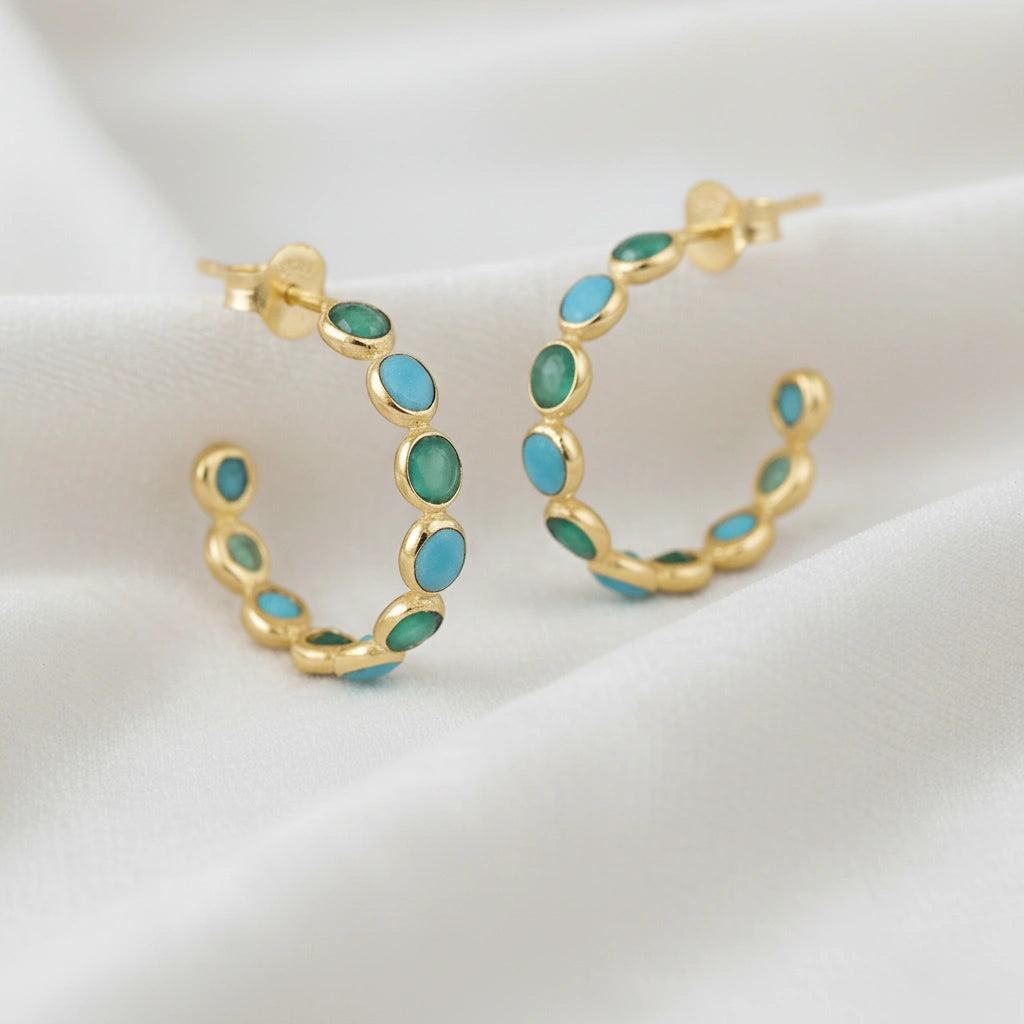 Gold vermeil turquoise hoop earrings with green onyx stones on a wrinkled off white velvet background angled for detail.