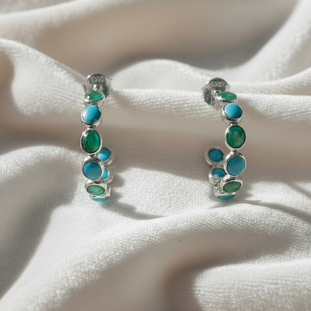 Sterling silver turquoise hoop earrings with green onyx stones on a wrinkled white velvet background angled for detail.