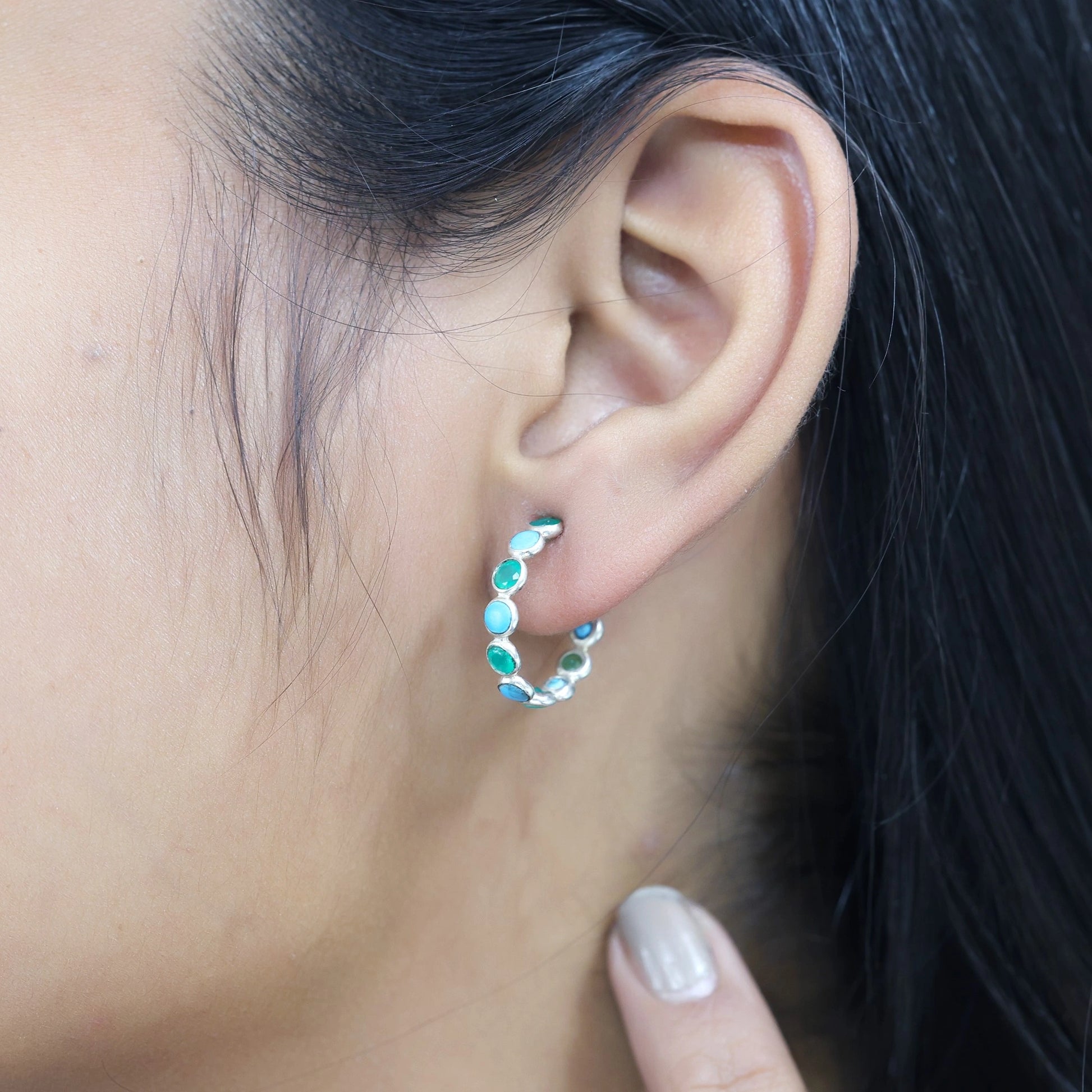 Side angle view of silver turquoise hoop earring with green stones worn on the ear with the hand touching the neck