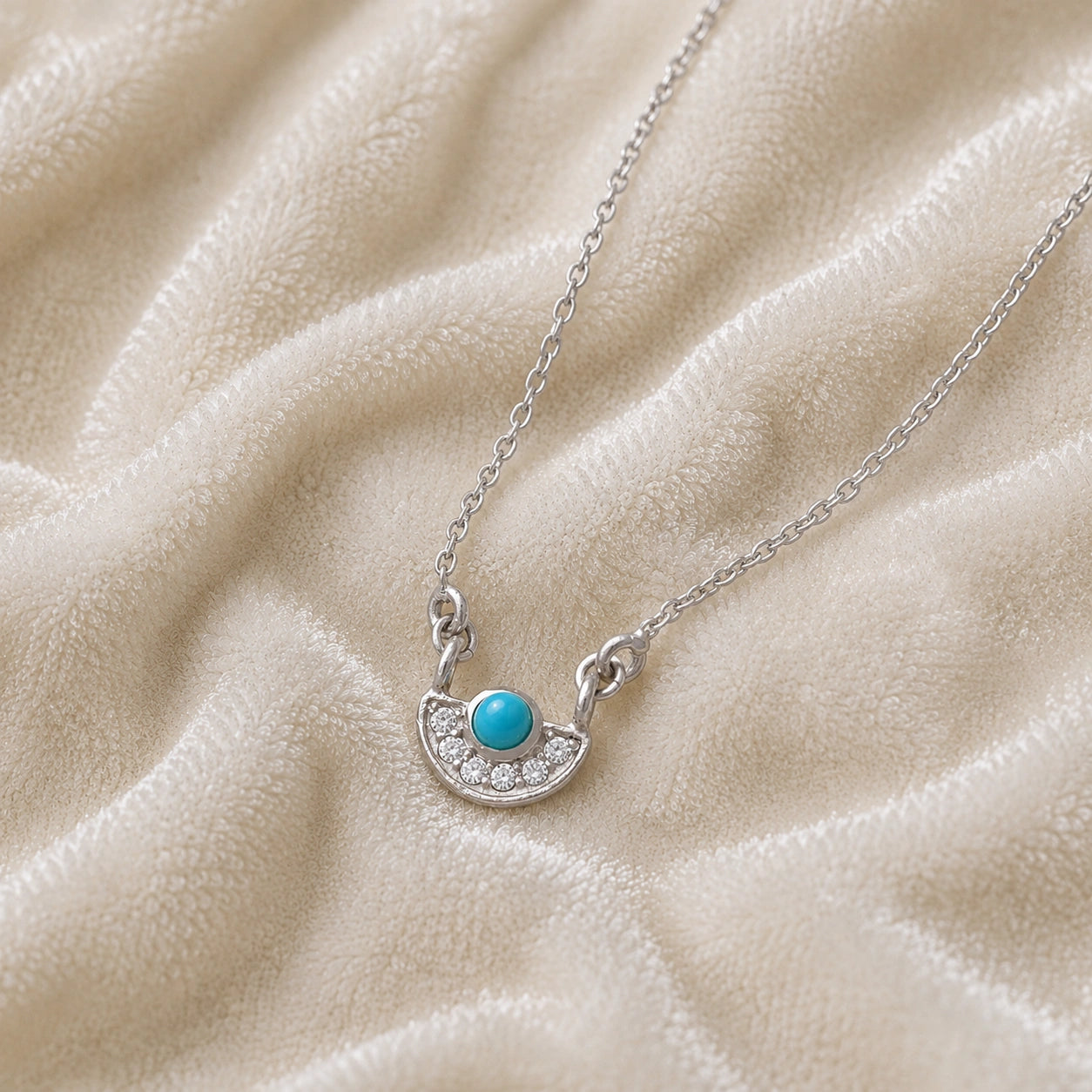Turquoise_necklace_in_sterling_silver_with_turquoise_and_CZ_stones_at_front_angle_view_on_soft_fabric_background