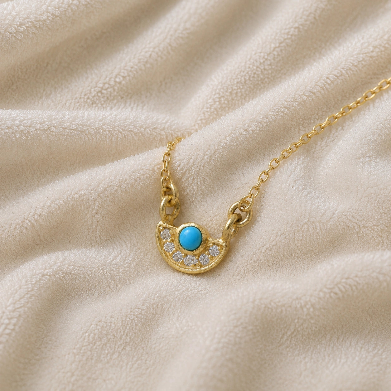 Turquoise_necklace_in_gold_plated_silver_with_turquoise_and_CZ_stones_at_slight_angle_view_on_soft_fabric_background