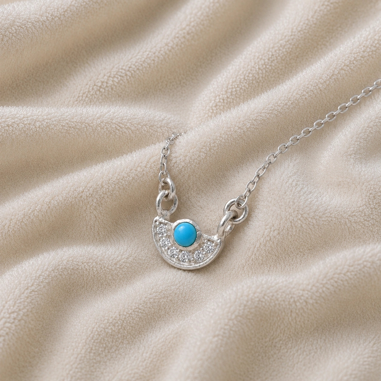 Turquoise_necklace_in_sterling_silver_with_turquoise_and_CZ_stones_at_slight_angle_view_on_soft_fabric_background