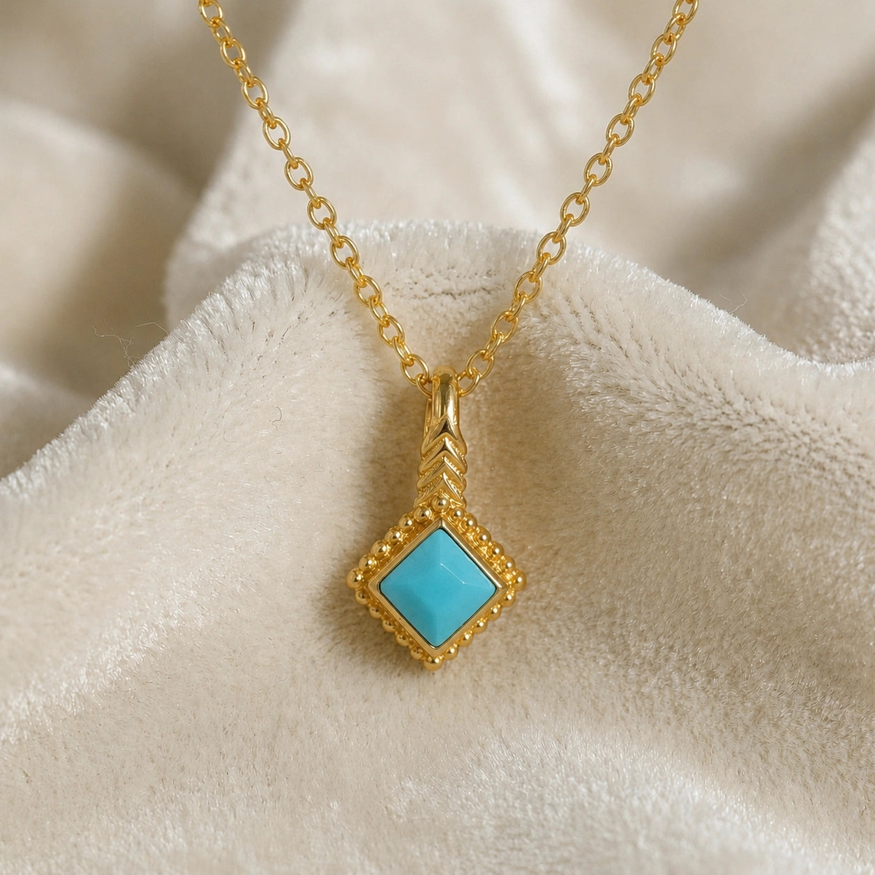 Birthstone_necklace_in_gold_plated_silver_with_square_cut_turquoise_pendant_in_front_angle_view_on_soft_white_fabric_background