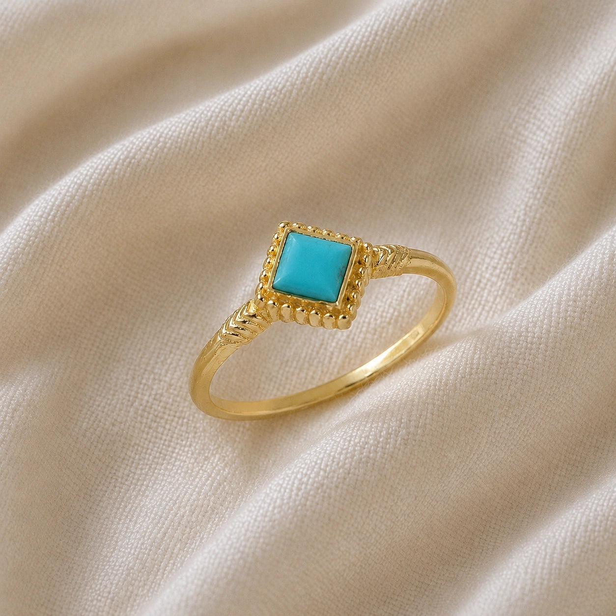 Princess_cut_ring_gold_plated_silver_with_square_turquoise_and_detailed_band_slightly_tilted_view_on_soft_fabric_background
