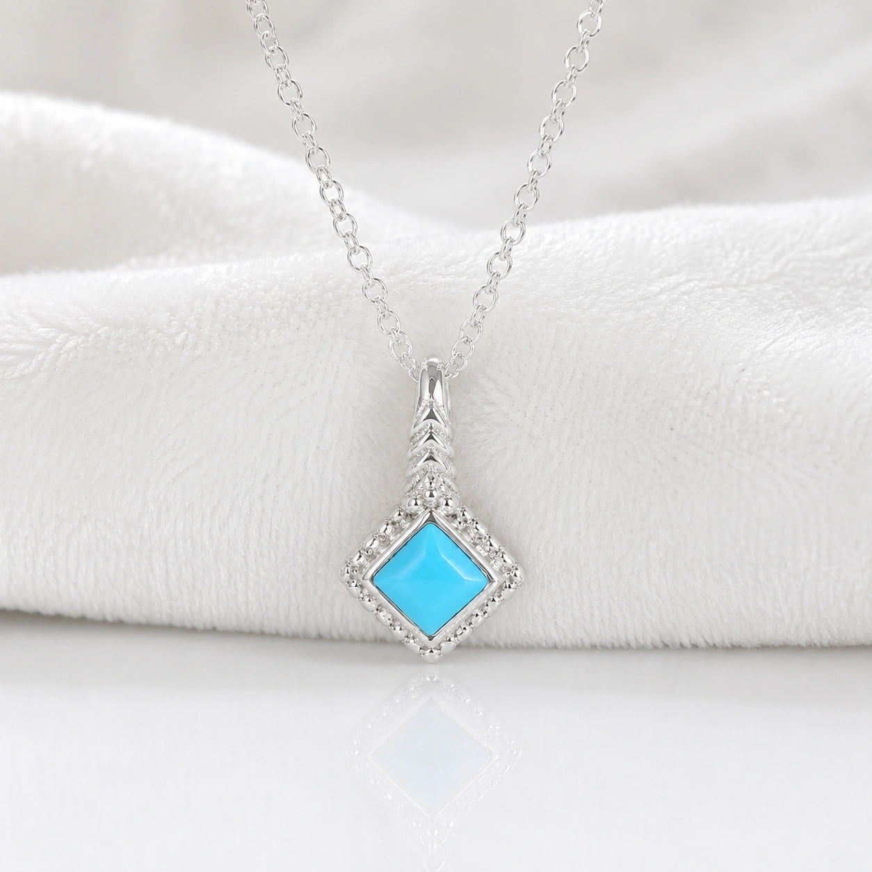 Birthstone_necklace_in_sterling_silver_with_square_cut_turquoise_pendant_in_front_angle_view_on_soft_white_fabric_background
