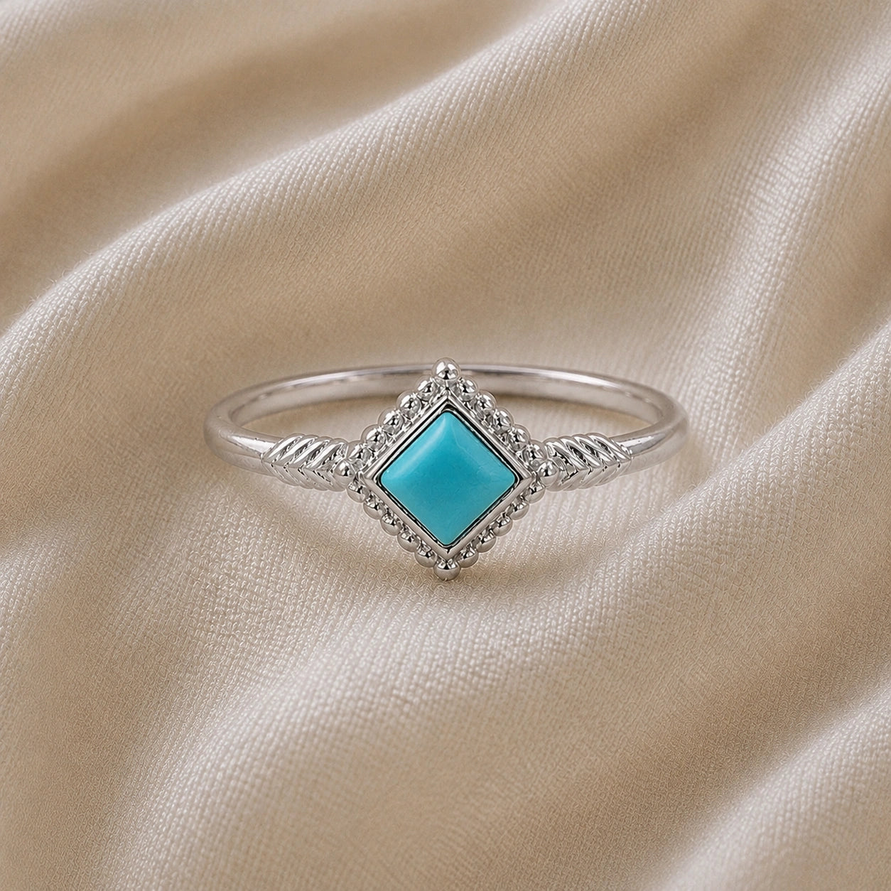 Princess_cut_ring_sterling_silver_with_square_turquoise_and_detailed_band_front_angle_view_on_soft_fabric_background