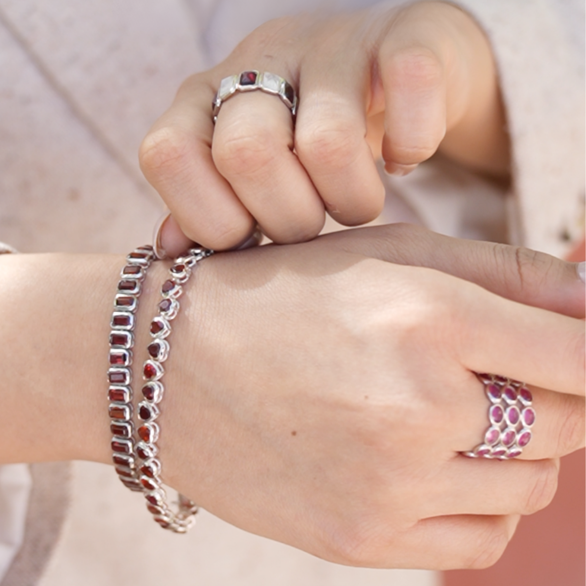 Silver ruby eternity band ring paired with bracelets on a hand wearing a jacket against a blurred background direct view.