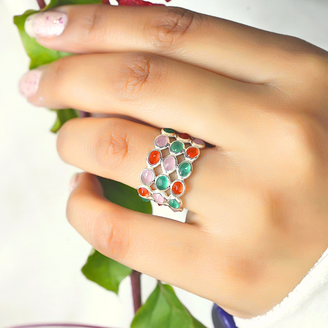 Silver multi stone ring with three bands of oval rose quartz carnelian green onyx stones on a wrinkled white velvet cloth.