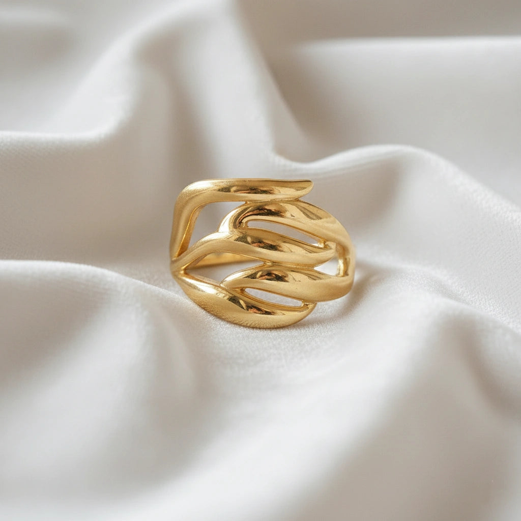 wave ring featuring a flowing gold-plated design as a statement ring over white fabric from a front view angle