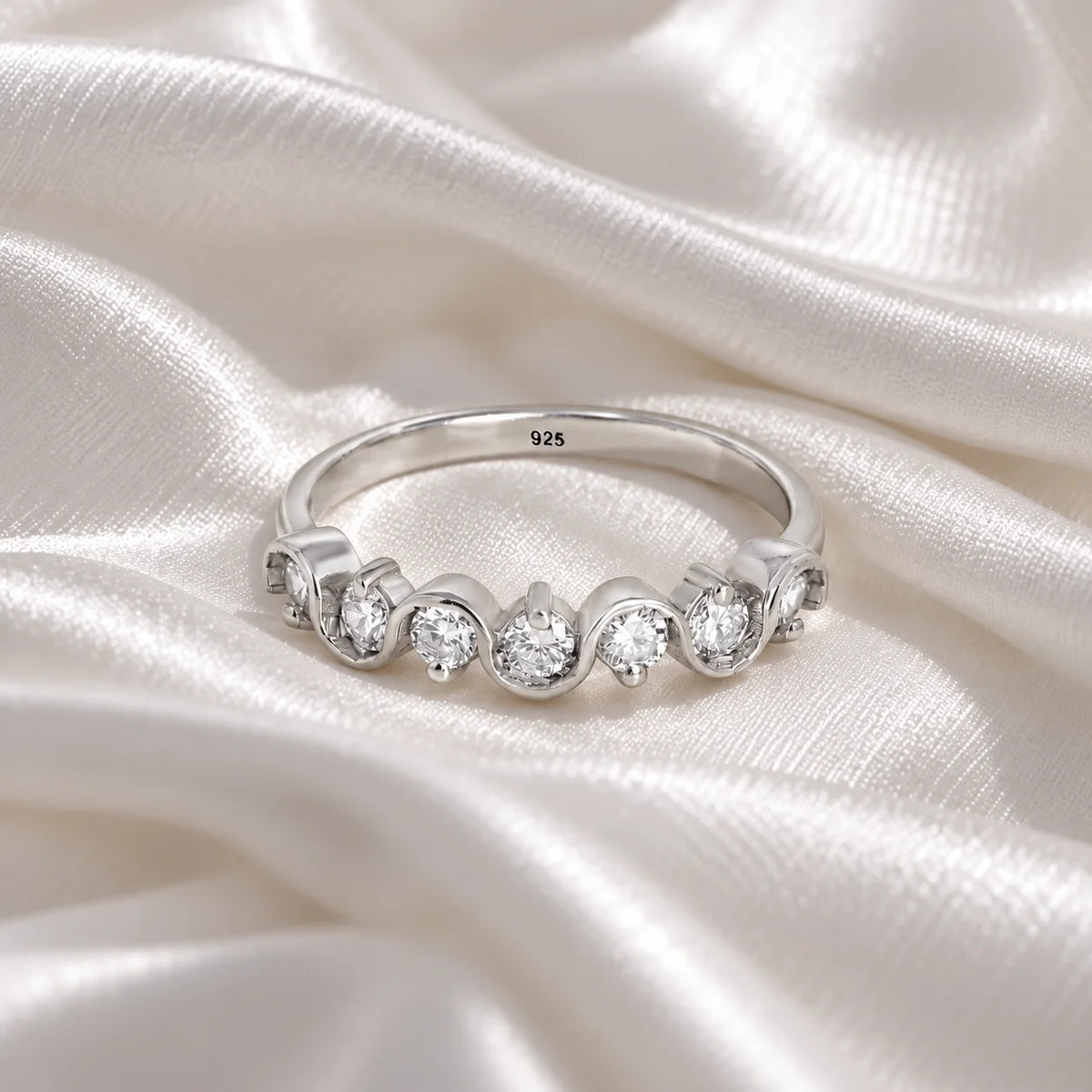 Wave_ring_in_sterling_silver_in_half_eternity_design_with_CZ_stones_at_front_angle_view_on_soft_fabric_background
