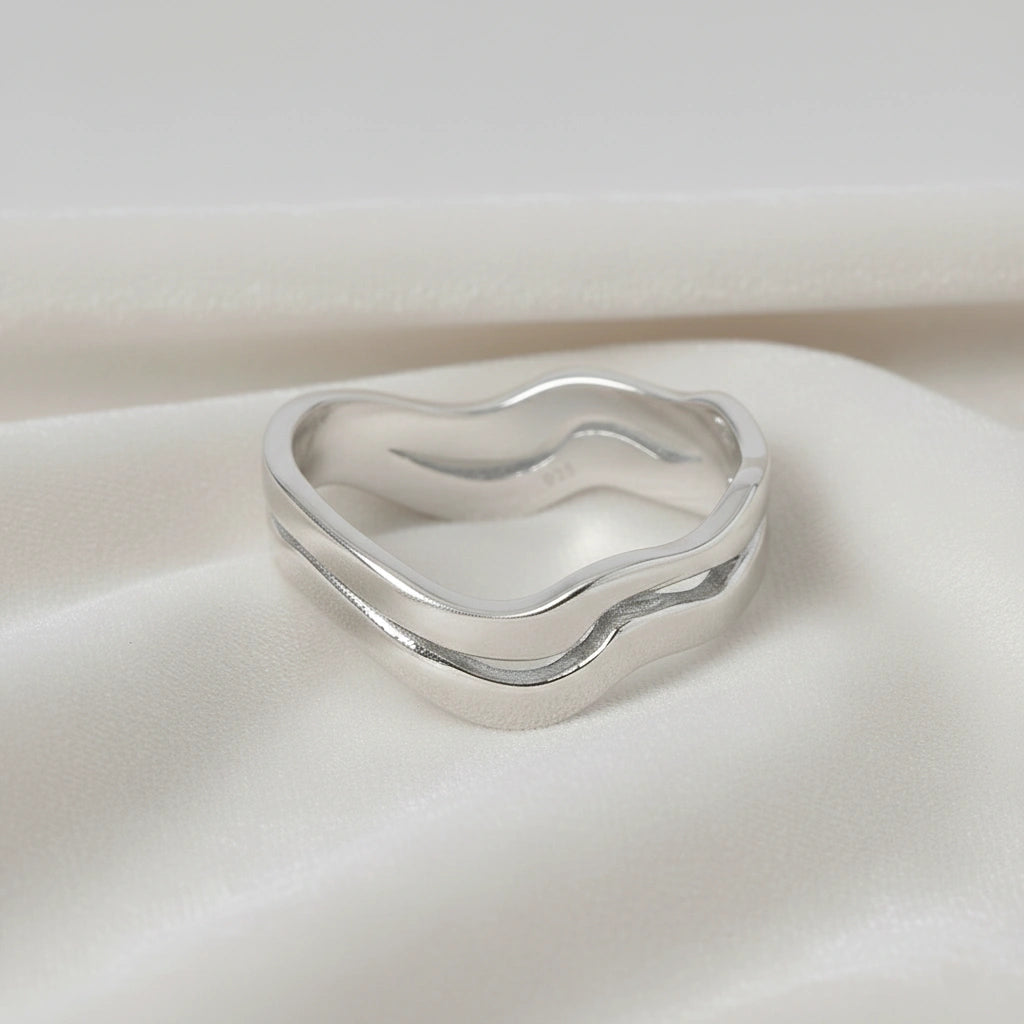 A straight angle view of a double layered wave ring silver band ring with an organic wavy design on a white fabric background