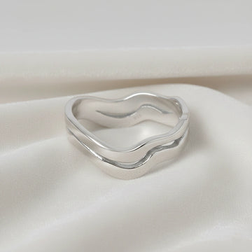 A straight angle view of a double layered wave ring silver band ring with an organic wavy design on a white fabric background