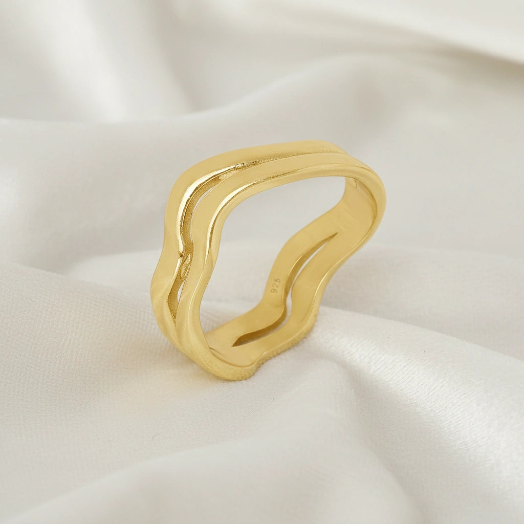 A side angle view of a gold-plated wave ring silver band ring with an organic wavy design set on a white fabric background