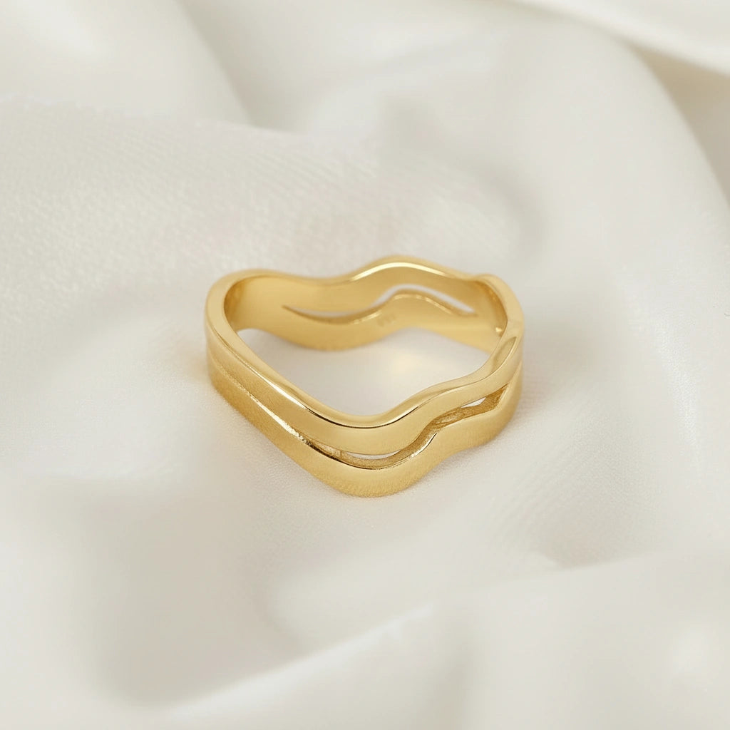 A straight angle view of a gold-plated wave ring silver band ring with an organic wavy design set on a white fabric background