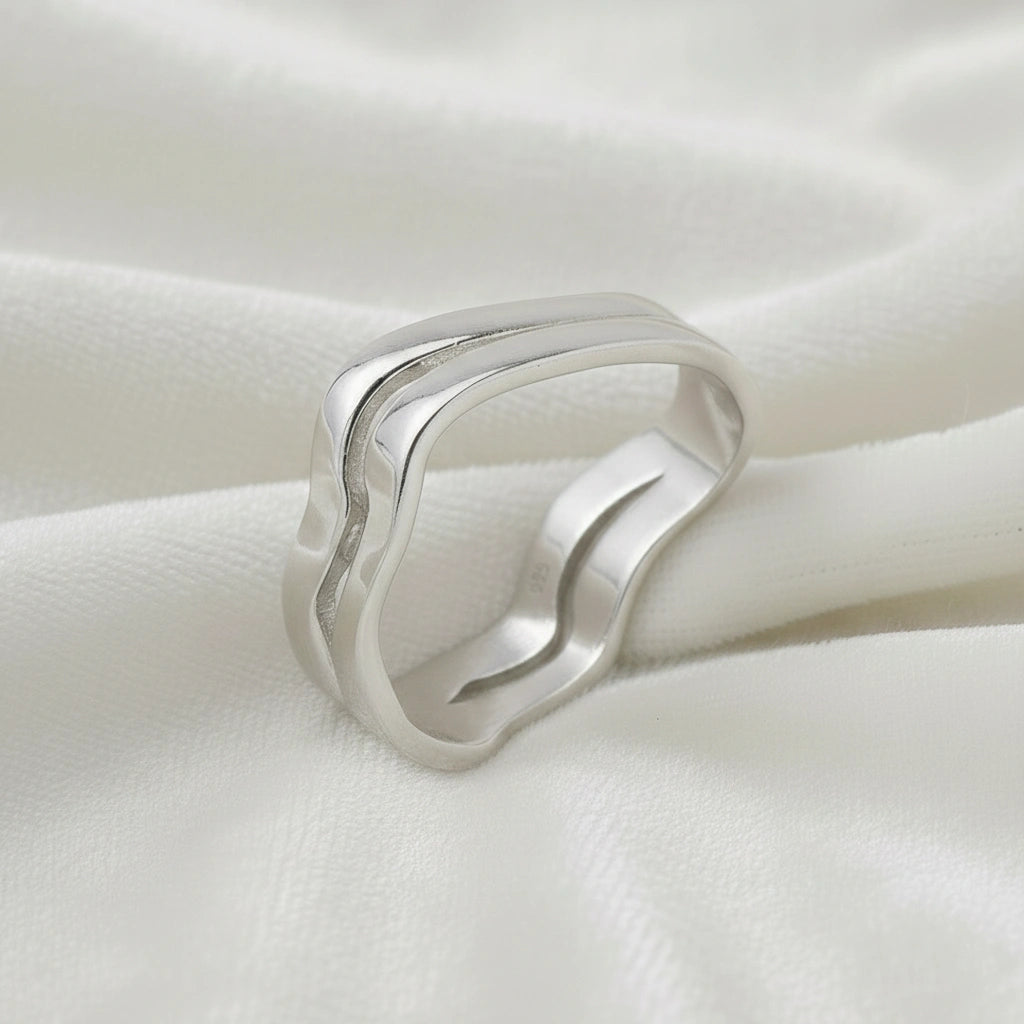 A side angle view of a double layered wave ring silver band ring with an organic wavy design on a white fabric background