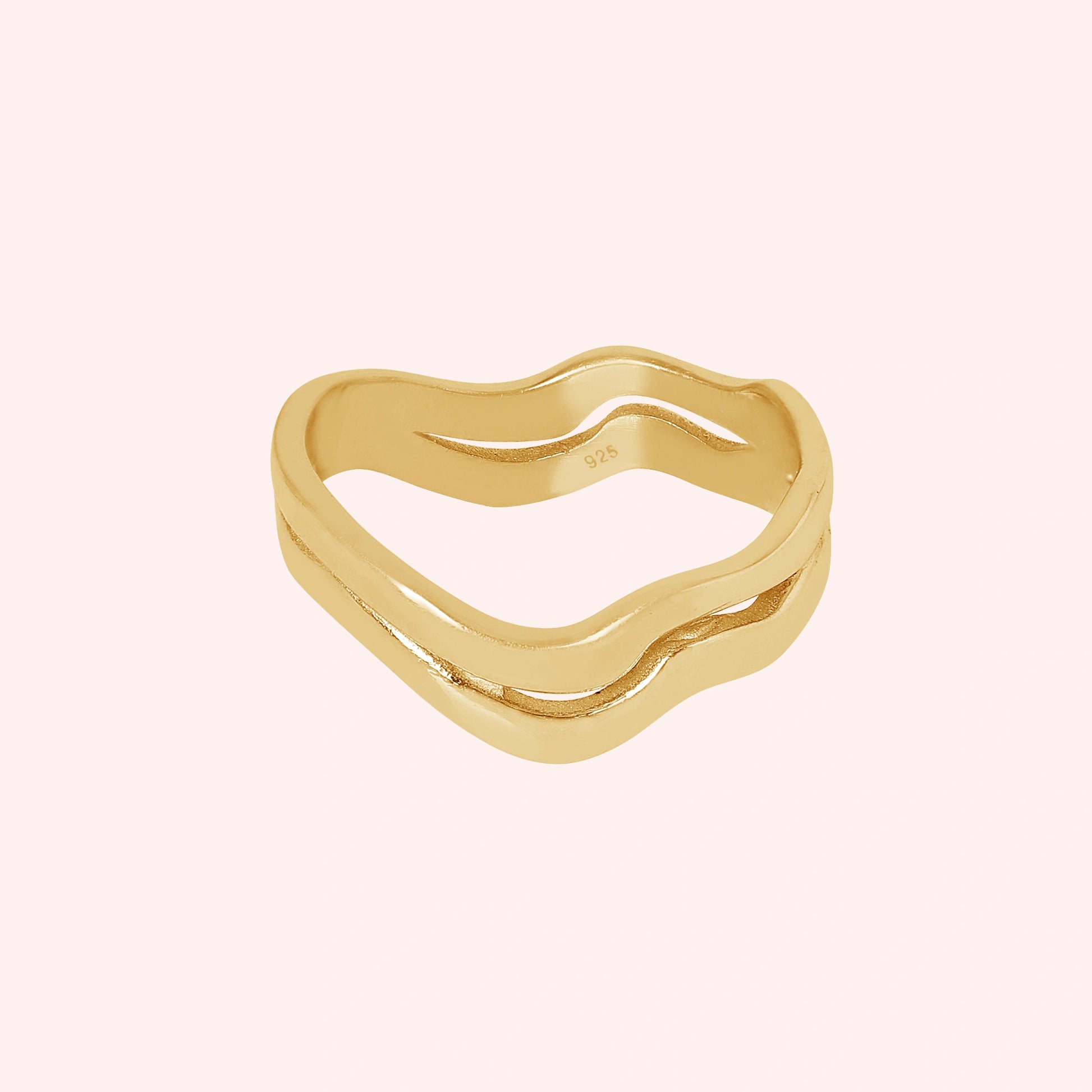 A straight angle view of a gold-plated wave ring silver band ring with an organic wavy design set on a soft pink background