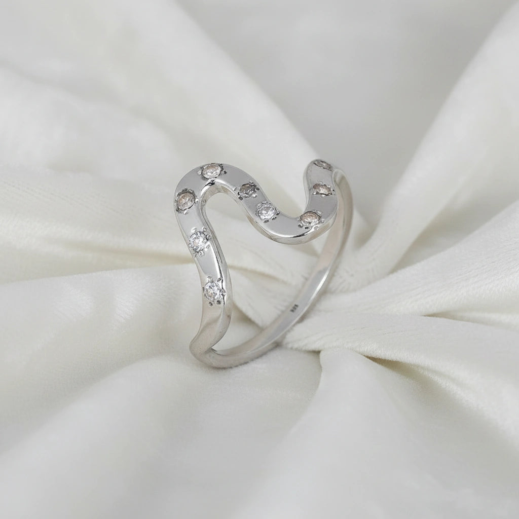 white topaz ring in sterling silver wave ring shown at a side angled view with curved band and stones on white fabric background