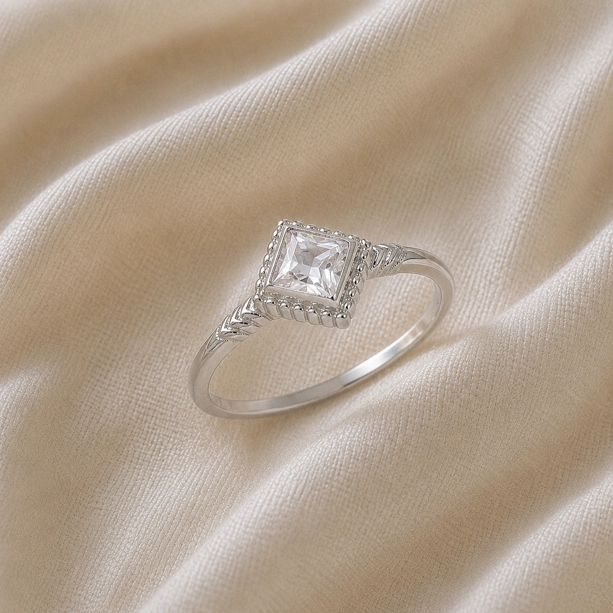 Princess_cut_ring_sterling_silver_with_square_white_topaz_and_detailed_band_slightly_tilted_view_on_soft_fabric_background