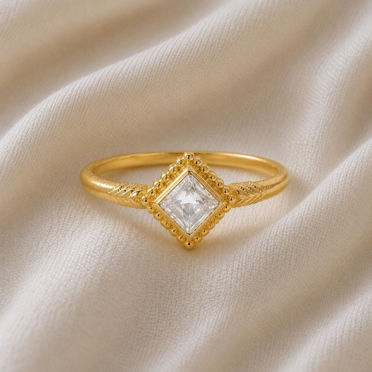 Princess_cut_ring_gold_plated_silver_with_square_white_topaz_and_detailed_band_front_angle_view_on_soft_fabric_background