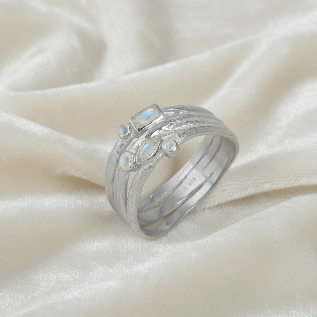Wide_band_ring_in_sterling_silver_with_multiple_moonstones_shown_in_slightly_angled_view_on_soft_fabric_background