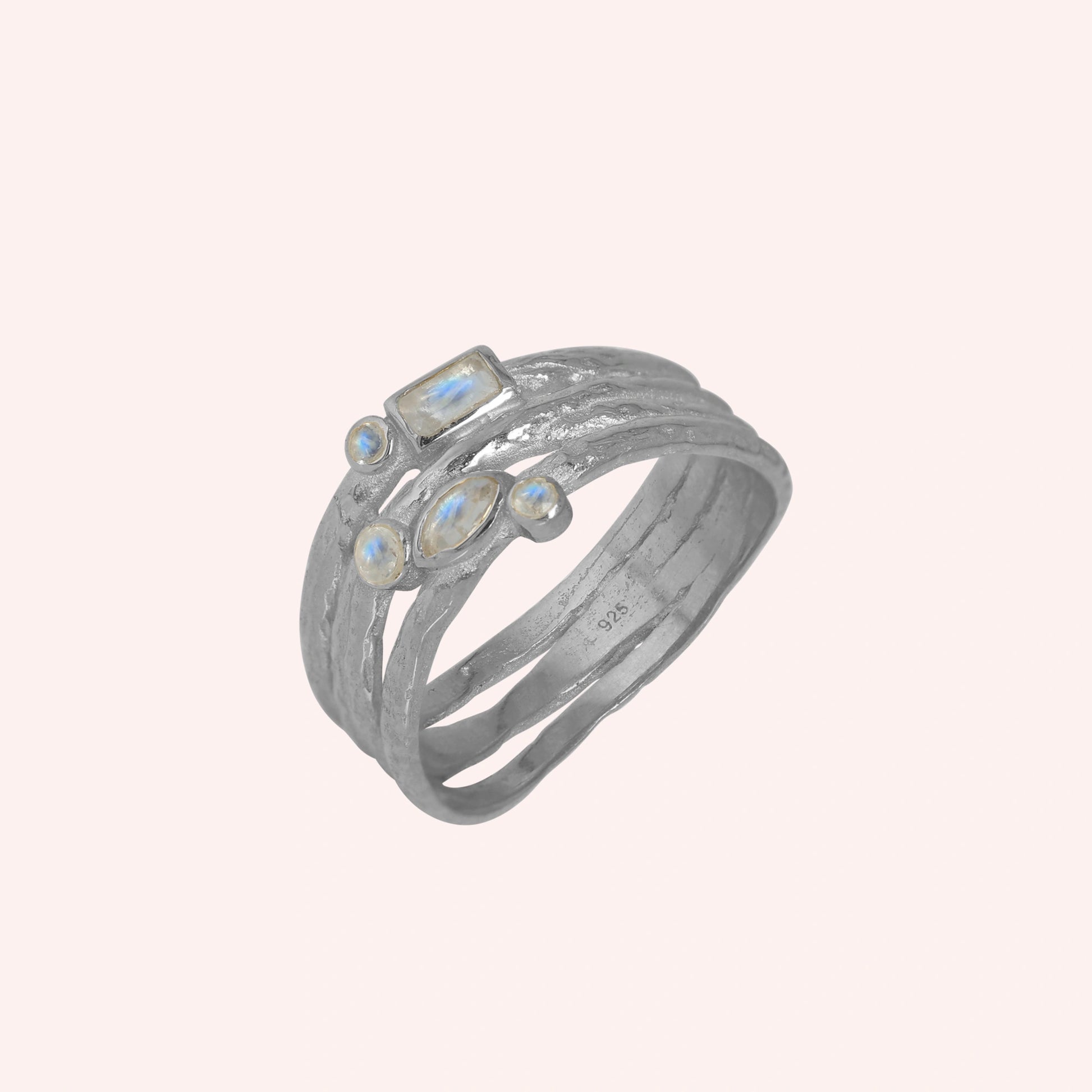 Wide_band_ring_in_sterling_silver_with_multiple_moonstones_shown_in_slightly_angled_view_on_solid_pink_background