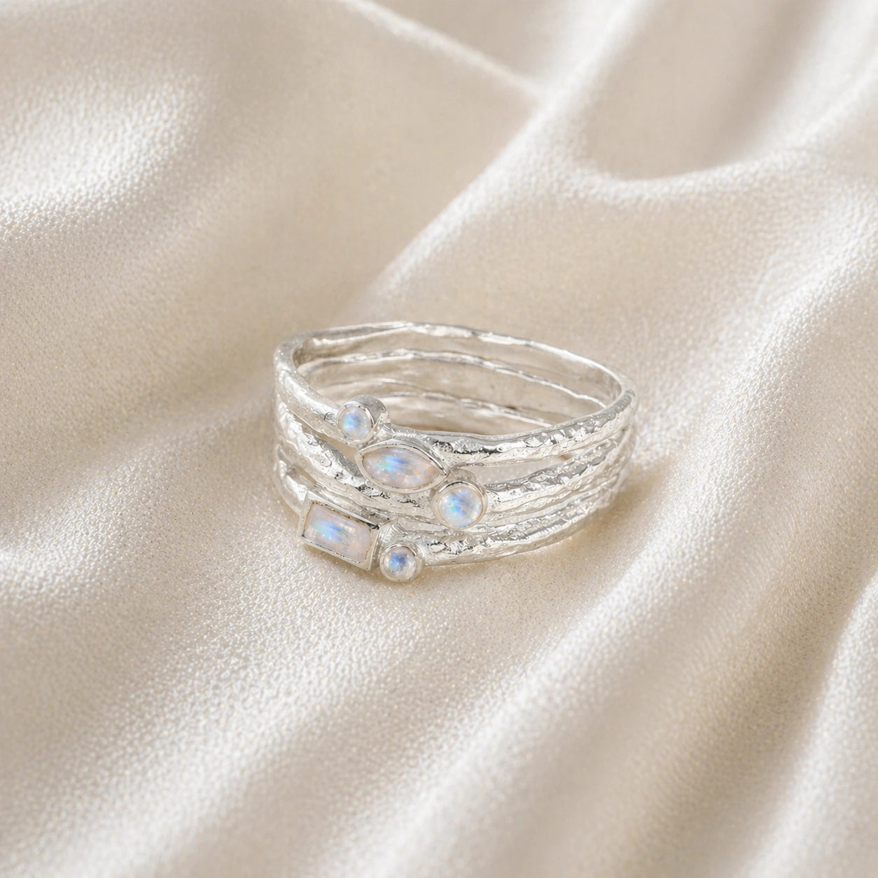 Wide_band_ring_in_sterling_silver_with_multiple_moonstones_shown_in_front_angle_view_on_soft_fabric_background