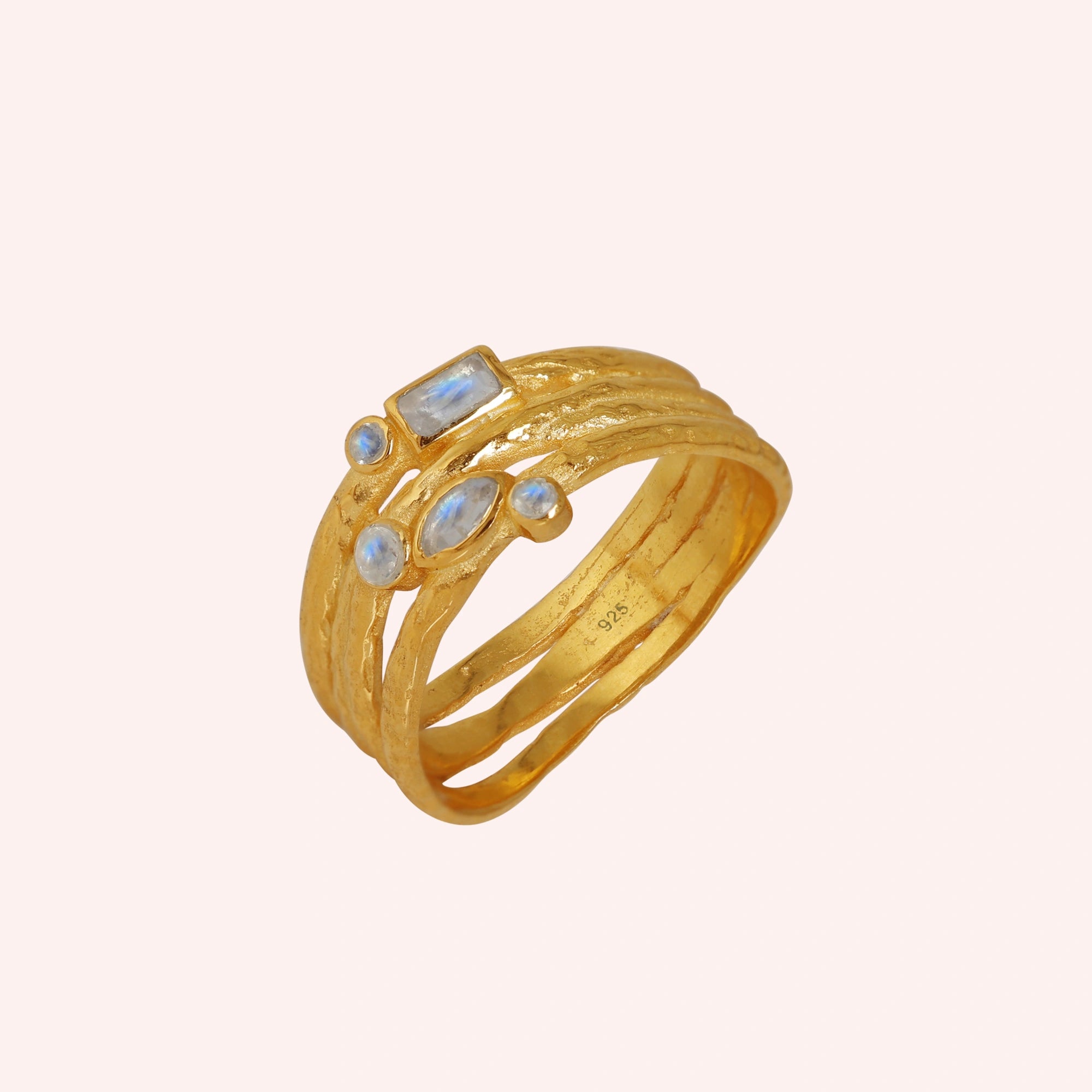 Wide_band_ring_in_gold_plated_silver_with_multiple_moonstones_shown_in_slightly_angled_view_on_solid_pink_background