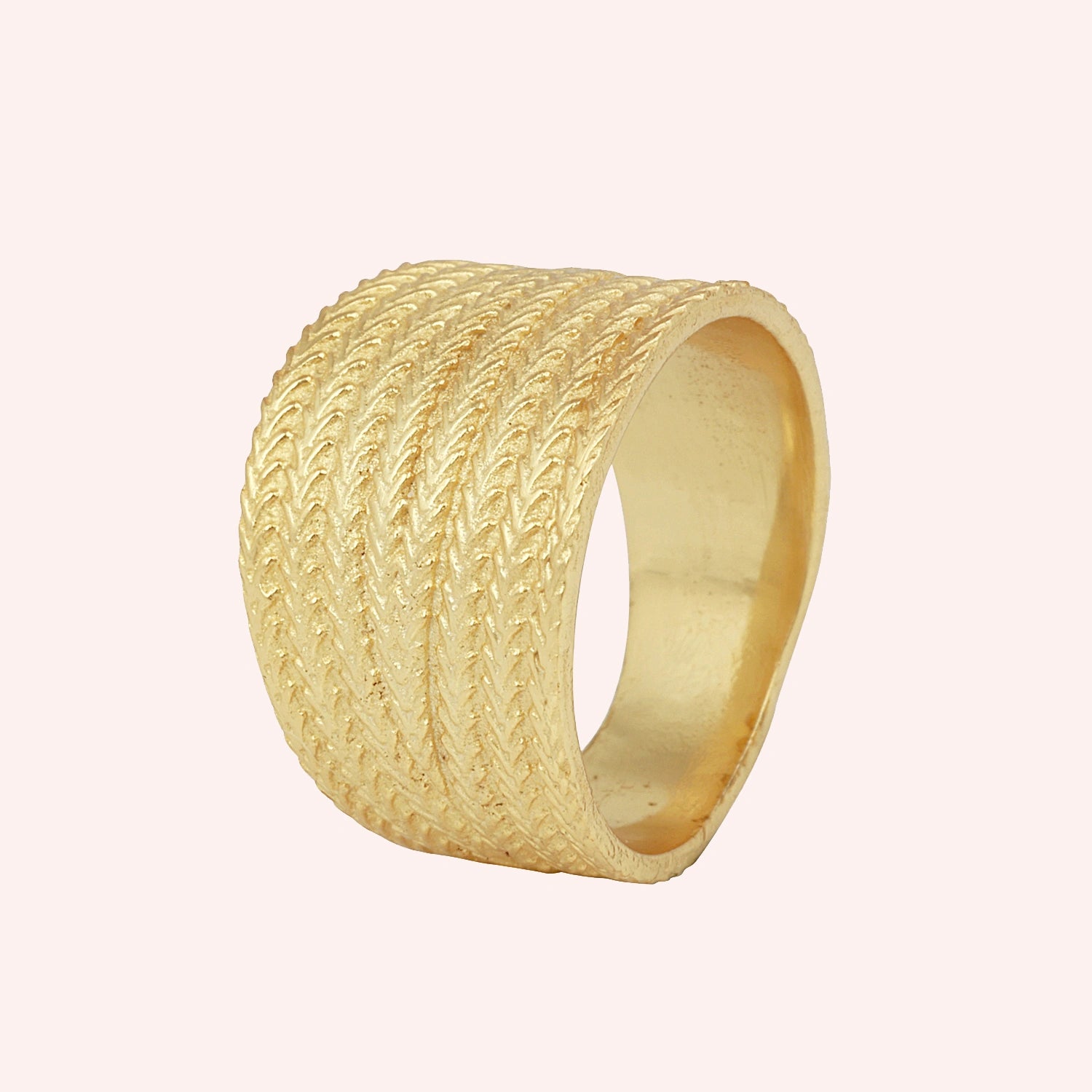 Wide_wedding_band_in_textured_gold_plated_silver_with_braided_pattern_in_slightly_angled_view_on_solid_pink_background