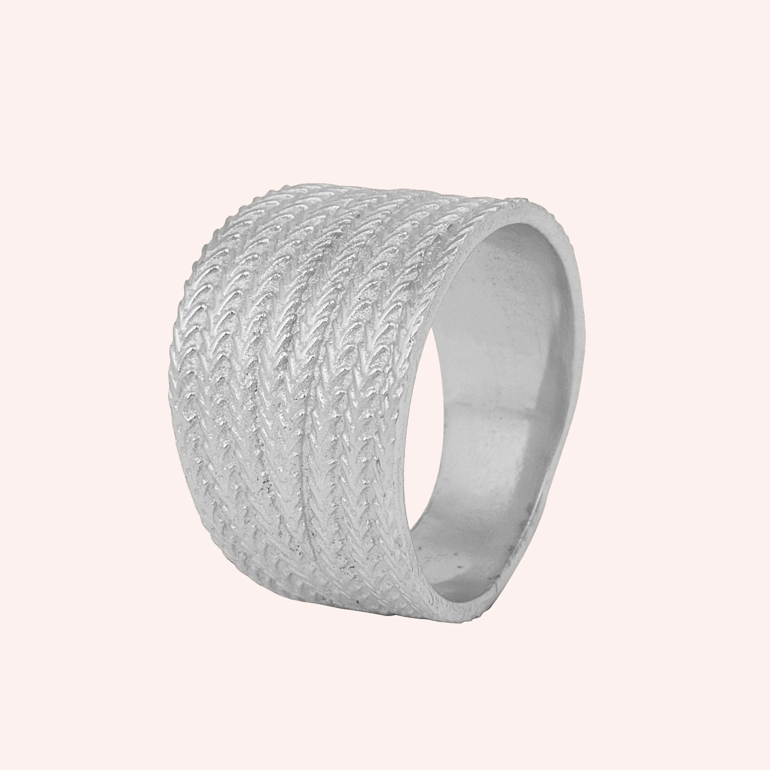Wide_wedding_band_in_textured_sterling_silver_with_braided_pattern_in_slightly_angled_view_on_solid_pink_background