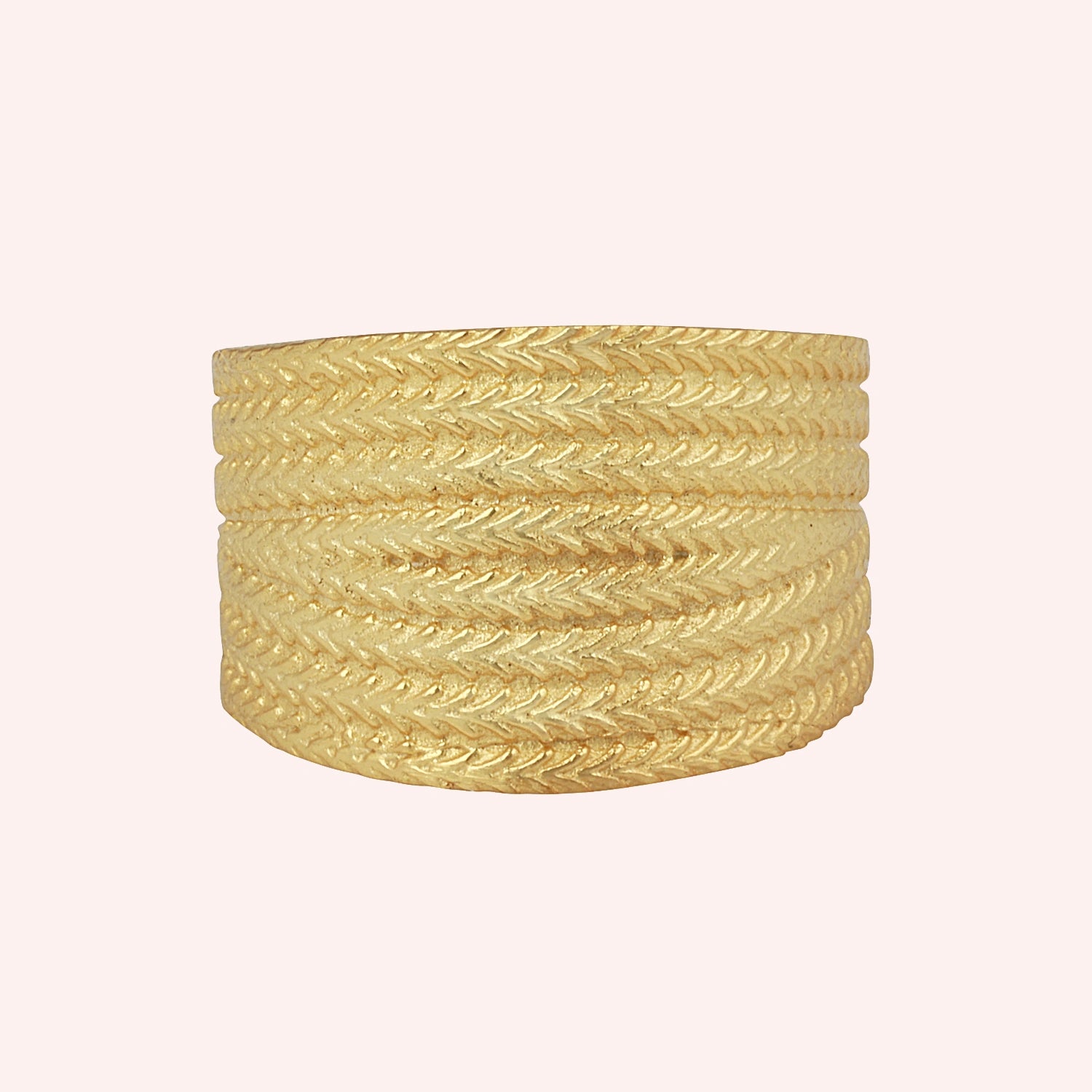 Wide_wedding_band_in_textured_gold_plated_silver_with_braided_pattern_in_front_angled_view_on_solid_pink_background