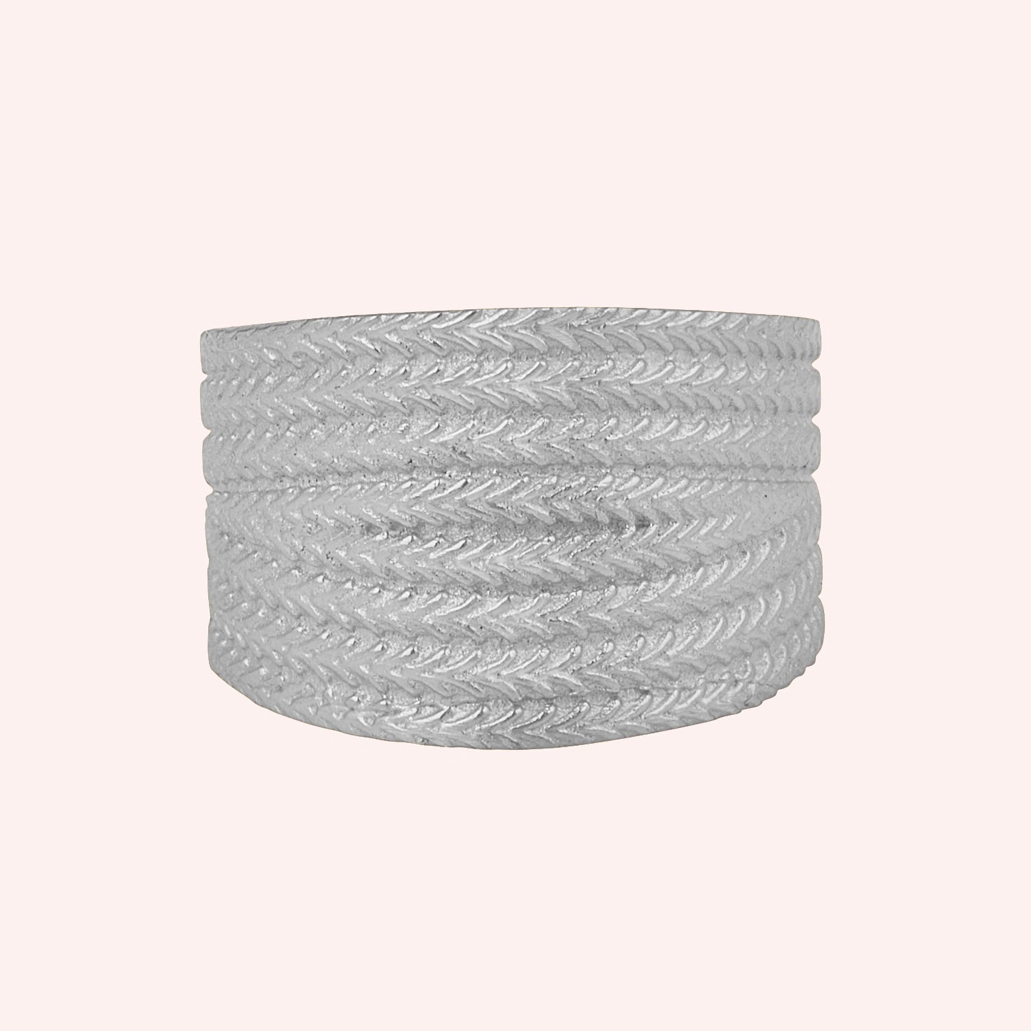 Wide_wedding_band_in_textured_sterling_silver_with_braided_pattern_in_front_angled_view_on_solid_pink_background