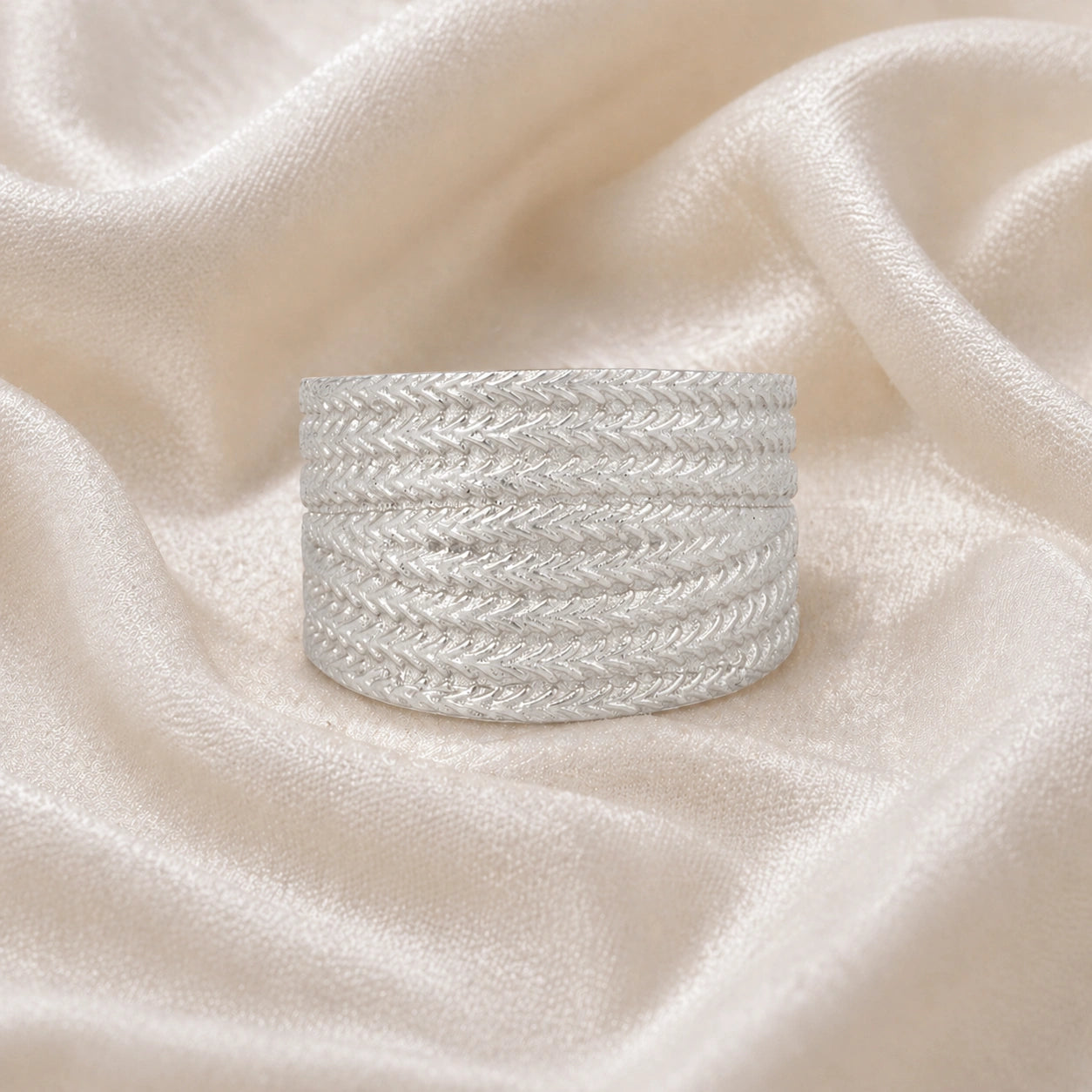 Wide_wedding_band_in_textured_sterling_silver_with_braided_pattern_in_front_angled_view_on_soft_fabric_background