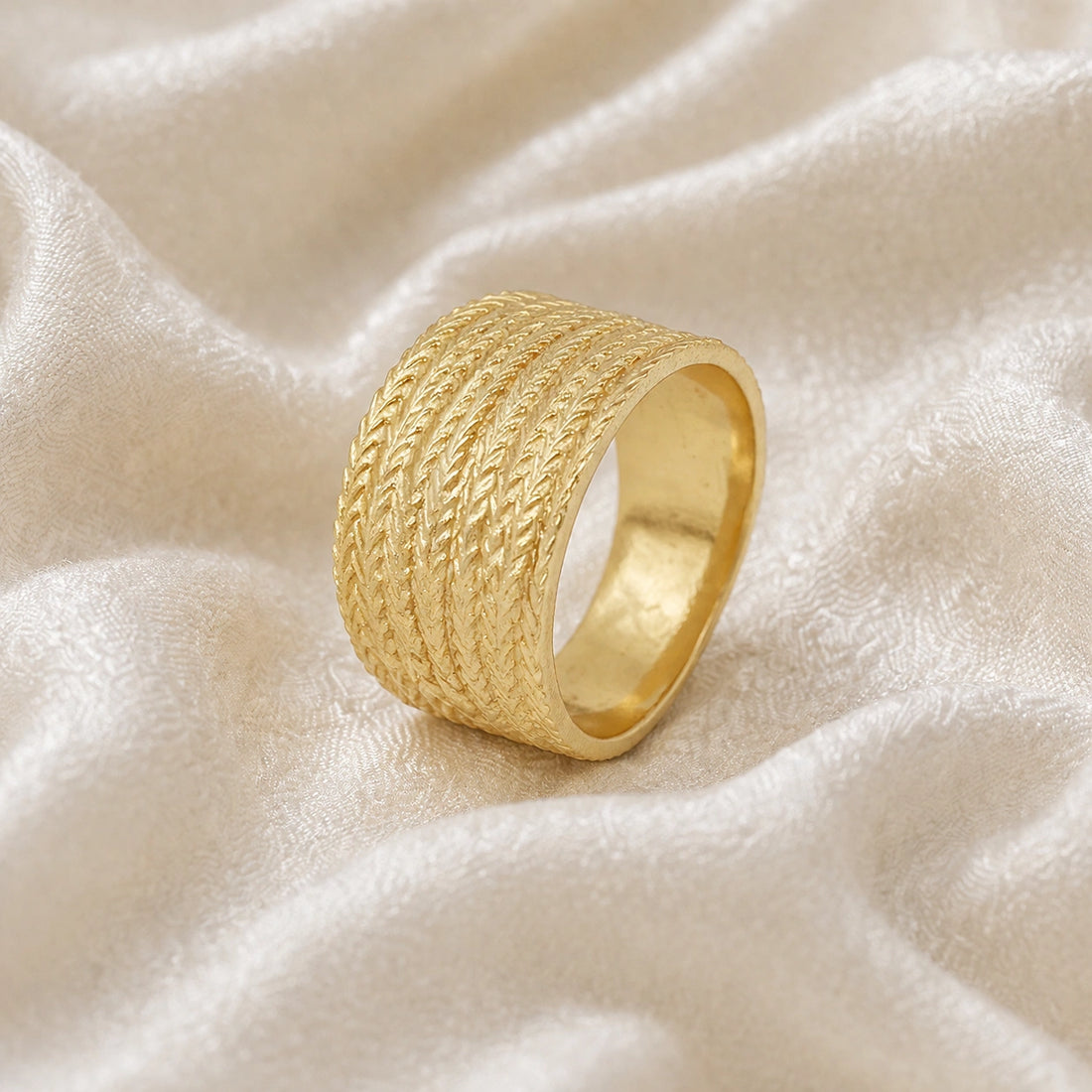 Wide_wedding_band_in_textured_gold_plated_silver_with_braided_pattern_in_slightly_angled_view_on_soft_fabric_background