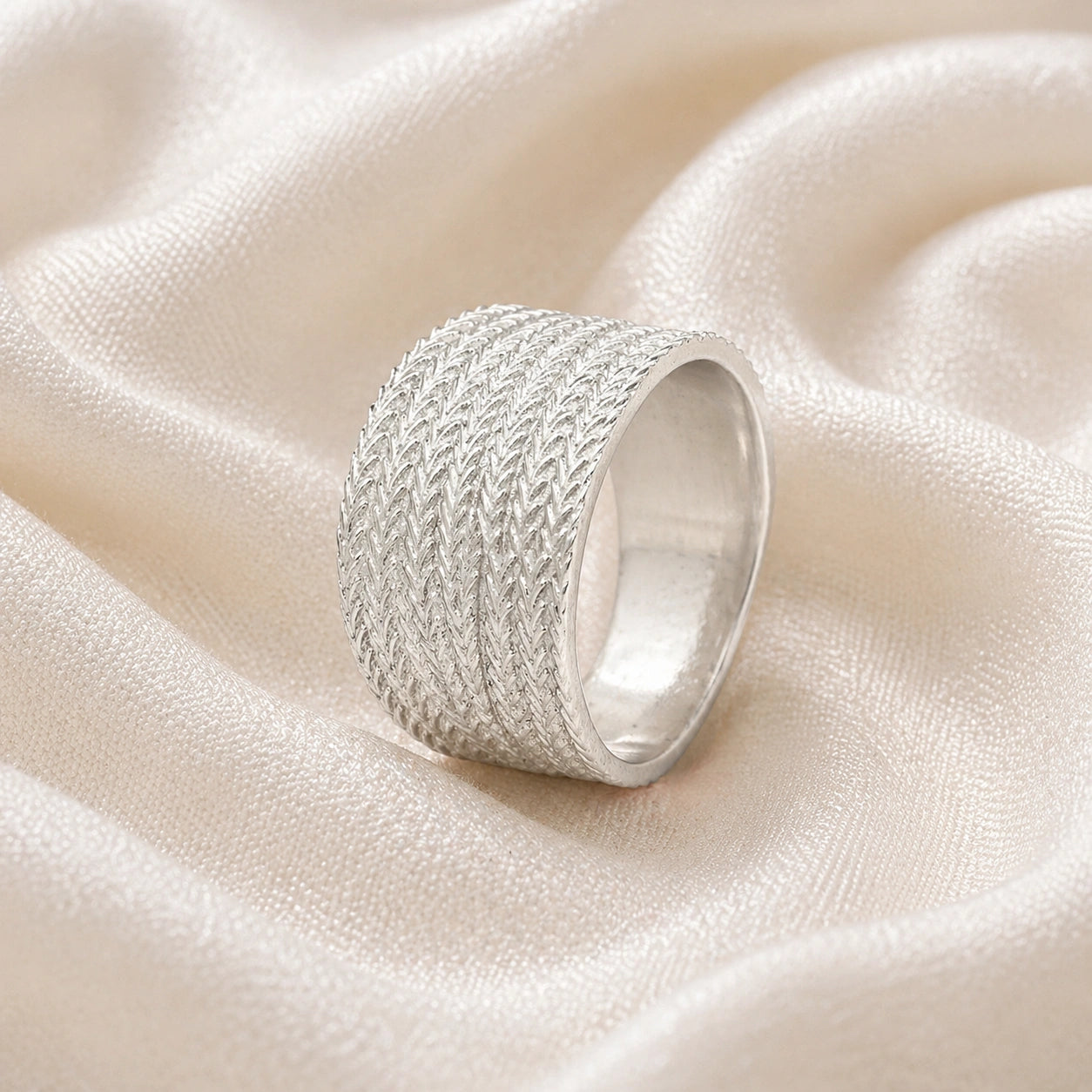 Wide_wedding_band_in_textured_sterling_silver_with_braided_pattern_in_slightly_angled_view_on_soft_fabric_background