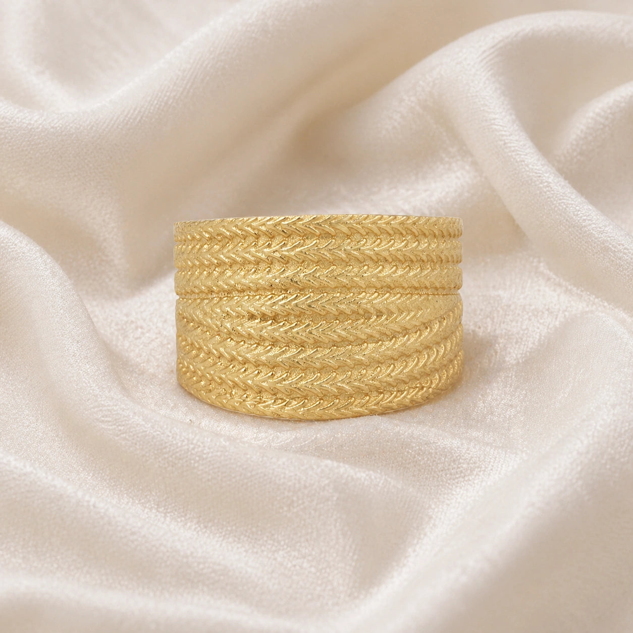 Wide_wedding_band_in_textured_gold_plated_silver_with_braided_pattern_in_front_angled_view_on_soft_fabric_background