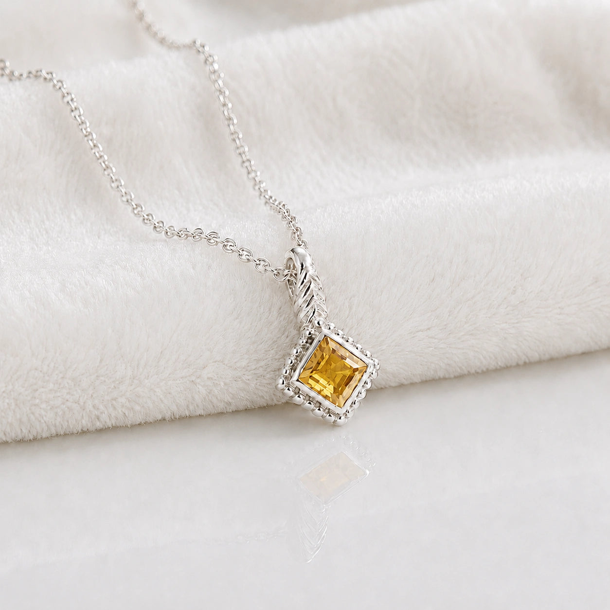 Birthstone_necklace_in_sterling_silver_with_square_cut_yellow_sapphire_pendant_in_slighlty_angled_view_on_soft_white_fabric_background
