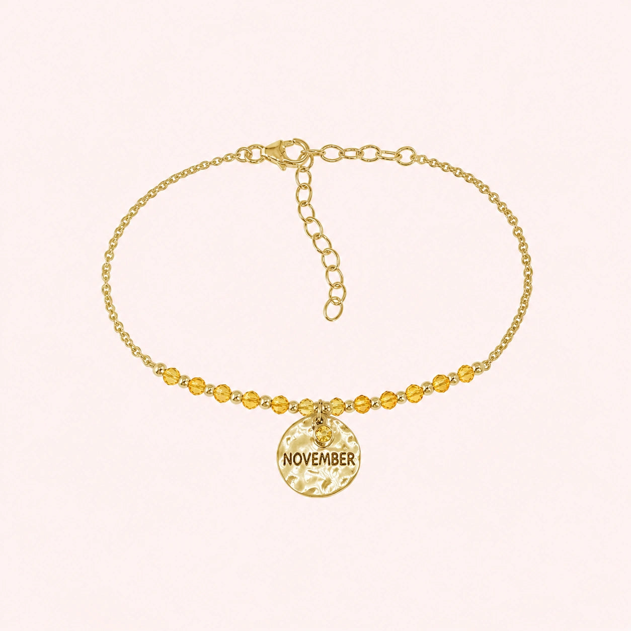 Birthstone_bracelet_in_gold_plated_silver_with_November_charm_and_yellow_topaz_beads_on_fine_chain_on_solid_pink_background