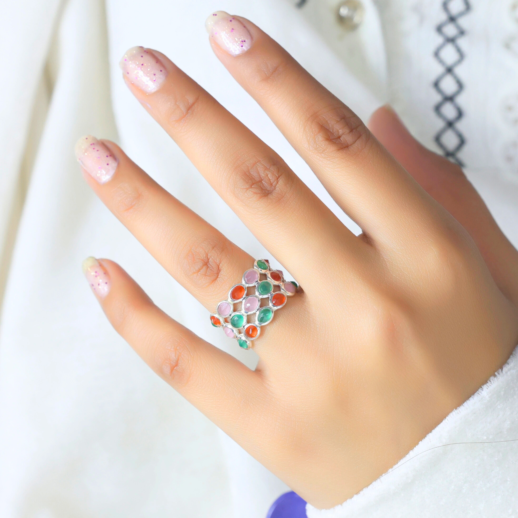 Silver multi stone ring with oval carnelian rose quartz green onyx gemstones worn on a hand against a white background.