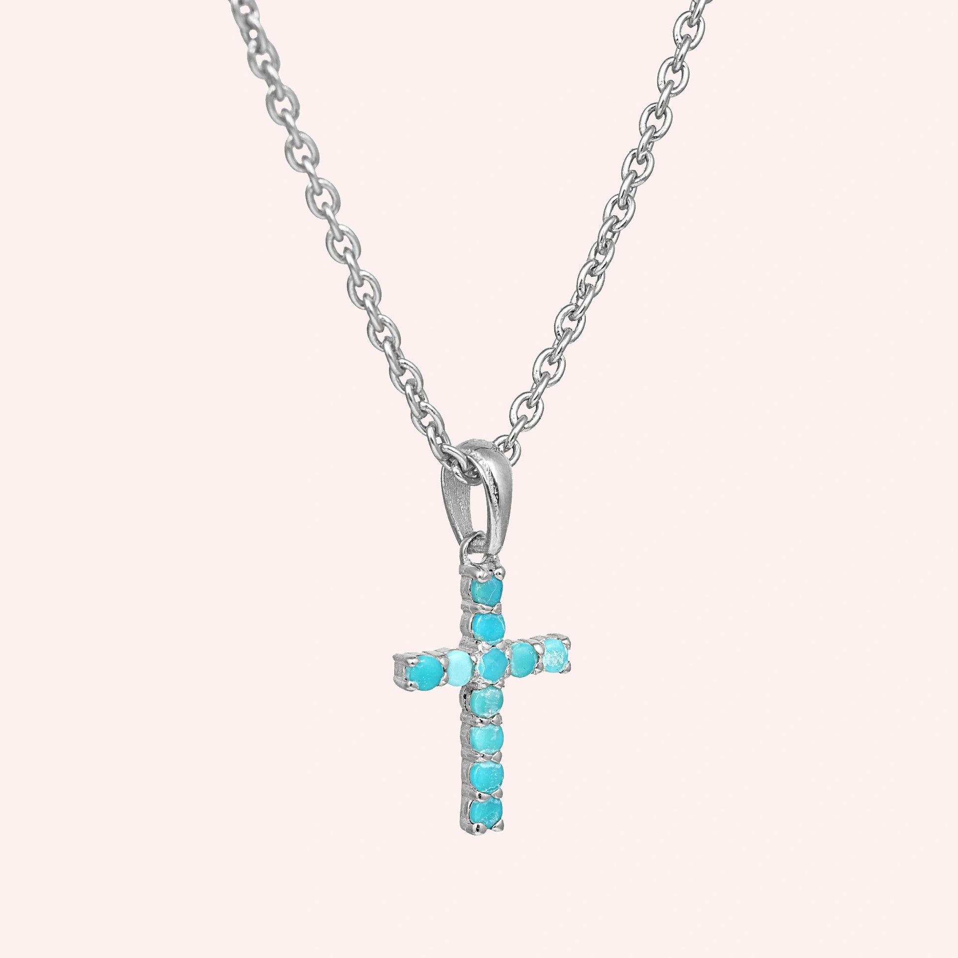 A front side angle of a sterling silver cross pendant necklace with turquoise cross necklace stones over a light pink backdrop